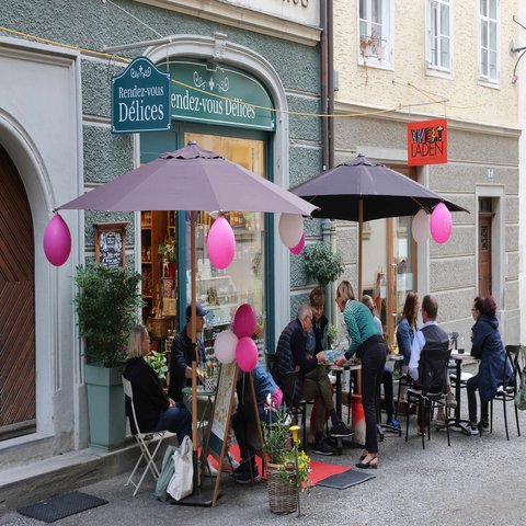 Vor einem kleinen Geschäft stehen Sonnenschirme mit Luftballons