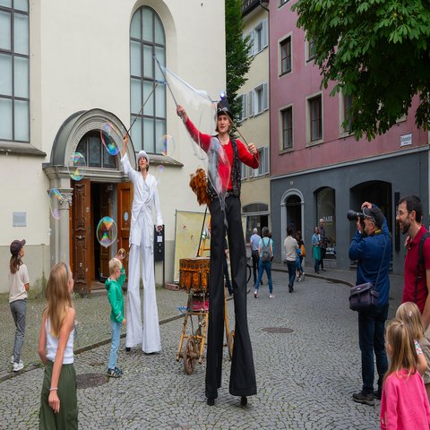 Zwei Männer auf Stelzen machen Seifenblasen
